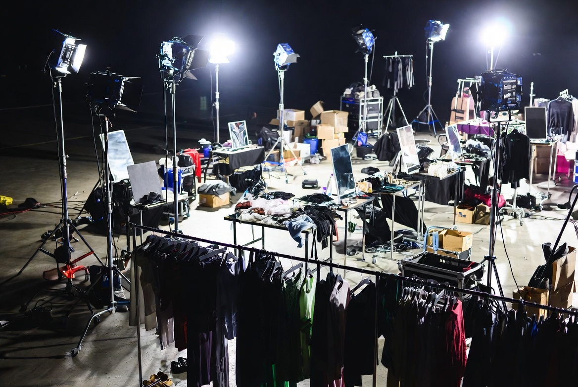 Backstage preparation area at a fashion event with garment racks, look boards, and technical equipment staged for show call