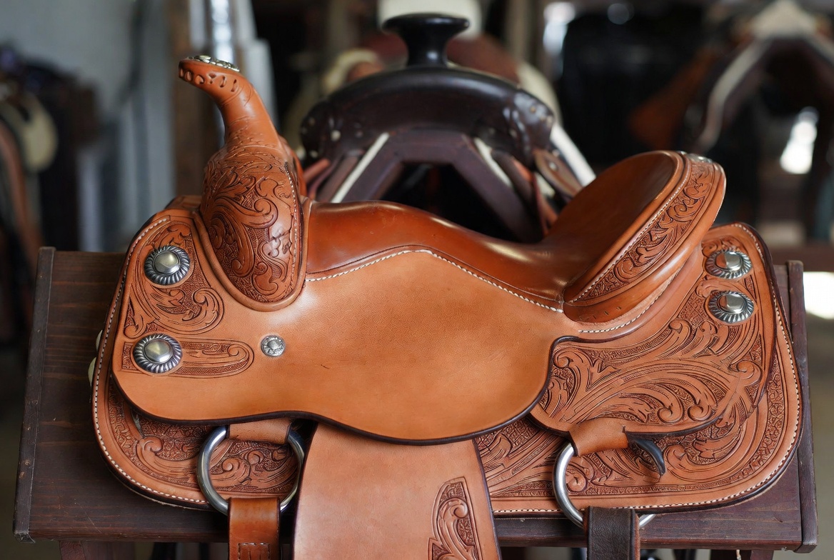 Hand-tooled western saddle on a wooden stand inside a tack room representing tack and equipment property exposure at a boarding and training stable