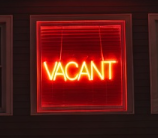 Bright red neon vacant sign glowing in a dark house window at night symbolizing an empty residence at risk under a homeowners policy vacancy clause