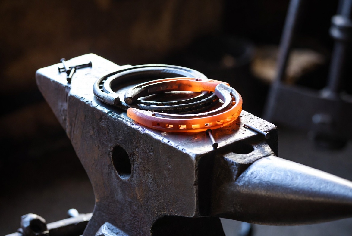 Heavy-duty farrier anvil with freshly forged horseshoes and nails laid out on a working surface representing the tools of professional farriery