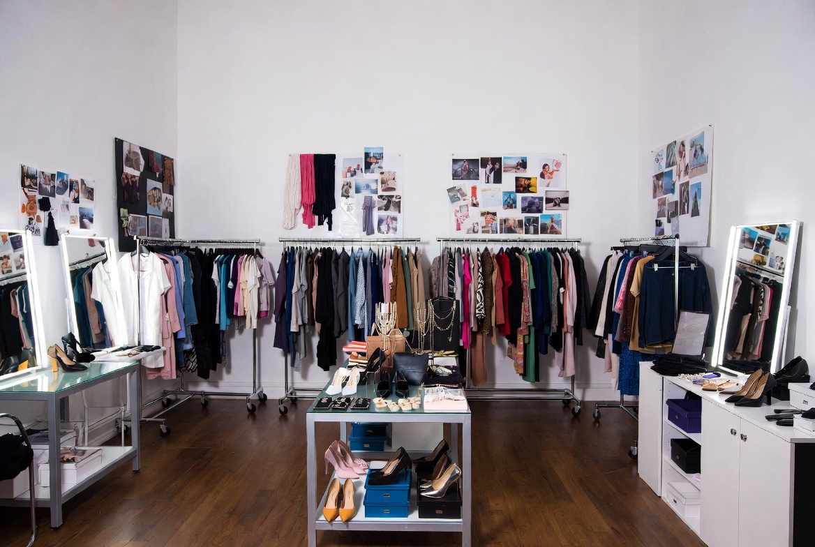 Professional fashion stylist creative workspace with curated outfit racks, mood boards, fabric swatches, and styling reference materials