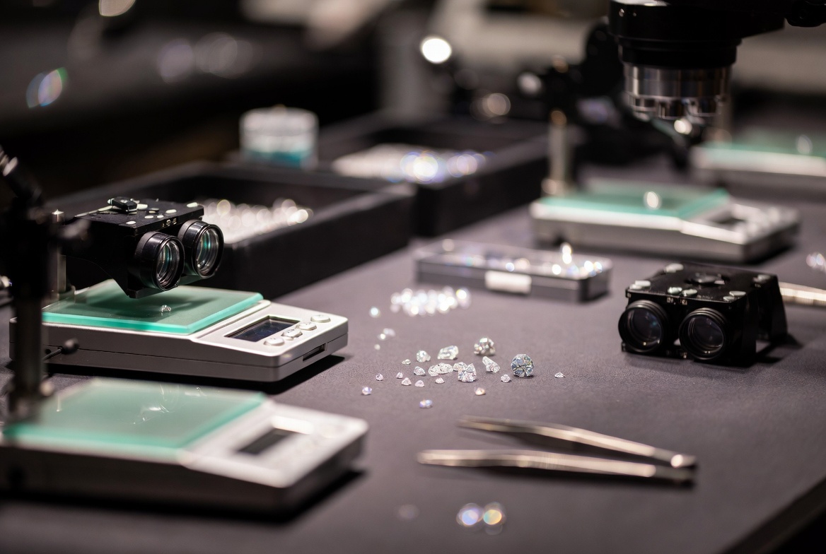 Secure diamond dealer trading room with loose gemstones under 10X magnification, digital scales, grading instruments, and parcel paper